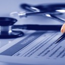 Hand holding a pen, filling in a form with a stethoscope in the background