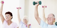 A group of smiling seniors lifting small dumbells in an exercise class