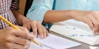 Hands writing notes with a pencil, with open text book alongside notebook