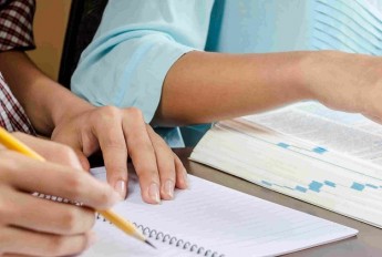 Hands writing notes with a pencil, with open text book alongside notebook