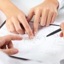 Two pairs of hands pointing out parts of a plan in an office environment