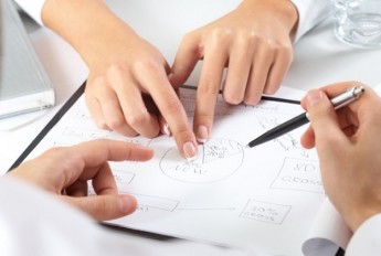 Two pairs of hands pointing out parts of a plan in an office environment