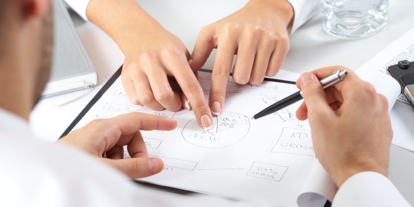 Two pairs of hands pointing out parts of a plan in an office environment