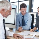 Three people sat around a desk discussing paperwork in front of them