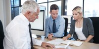 Three people sat around a desk discussing paperwork in front of them
