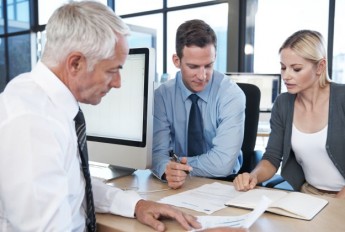 Three people sat around a desk discussing paperwork in front of them
