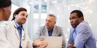 Doctor in a meeting with three others, laptop open alongside him