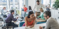 Man and woman leaning in discussing paperwork with office scene in the background